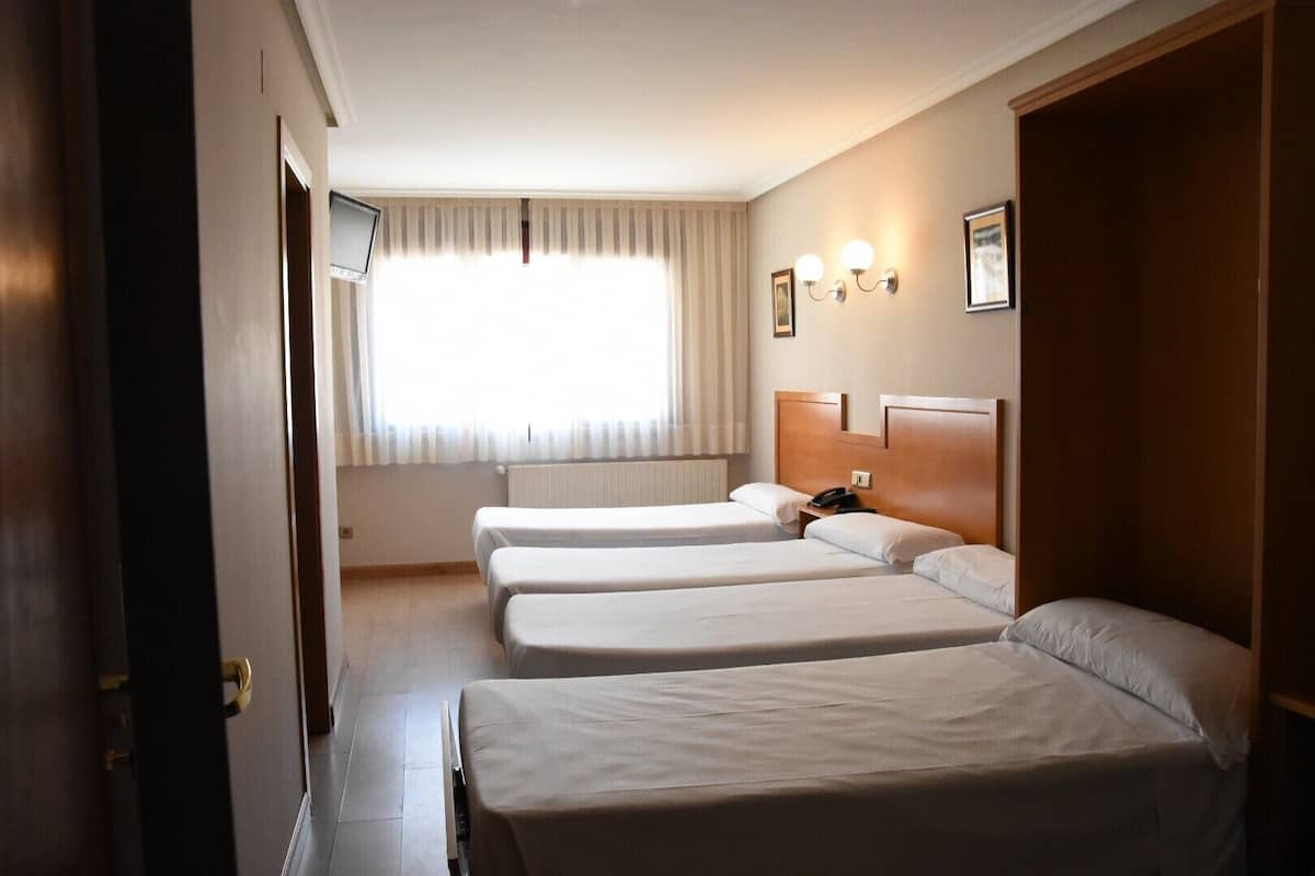 Habitación de hotel con tres camas individuales, teléfono en la mesita de noche y ventana con cortinas.