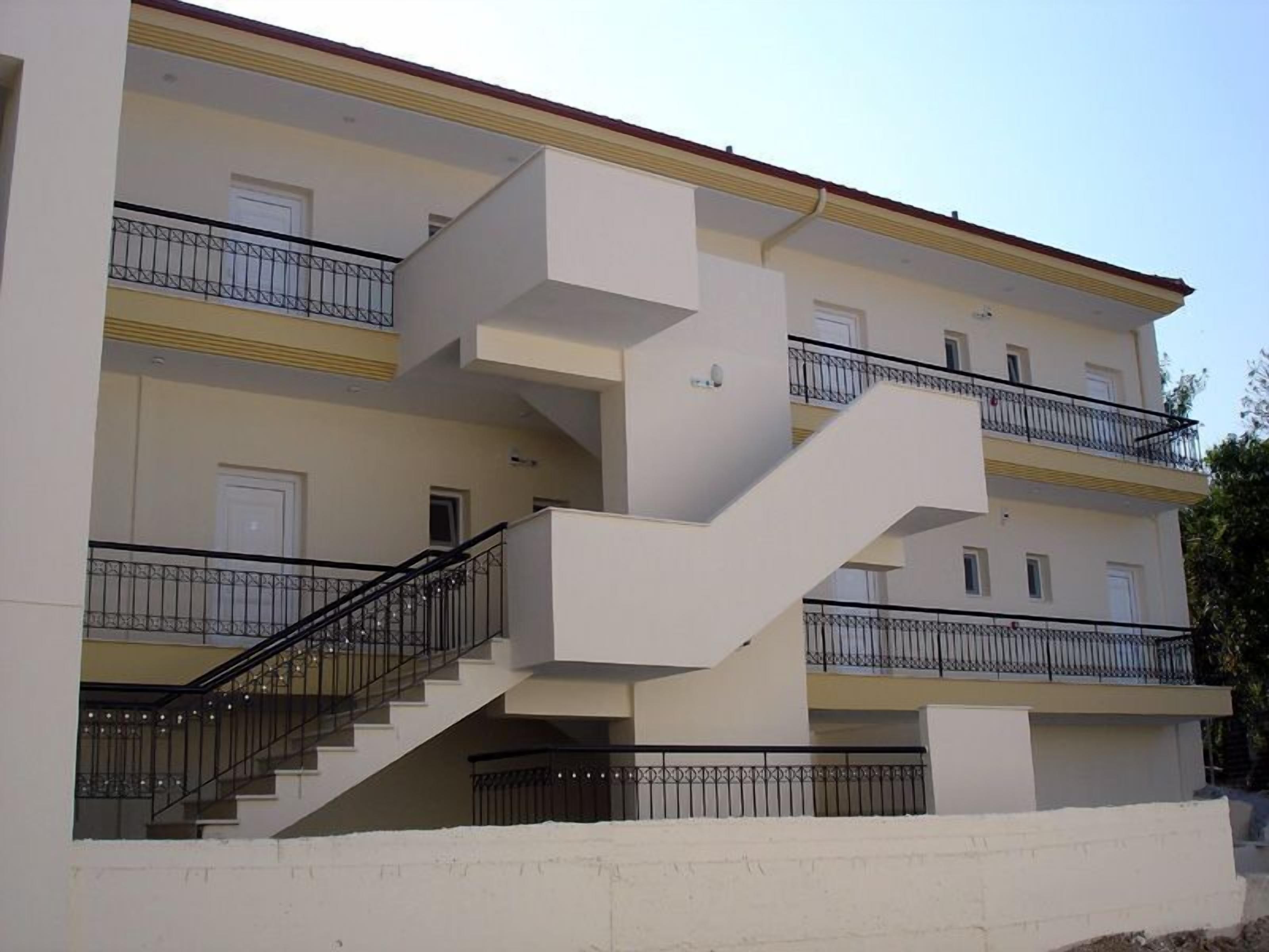A multi-story building with a central staircase, balconies on each floor, and a flat roof.