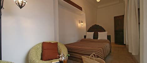 A bedroom with two beds, a wicker chair, a bedside table with a lamp, and a woven basket.