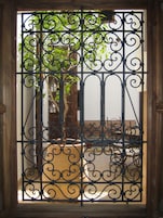Una reja de hierro forjado con un diseño decorativo, que da acceso a un patio con una mesa y sillas de madera.