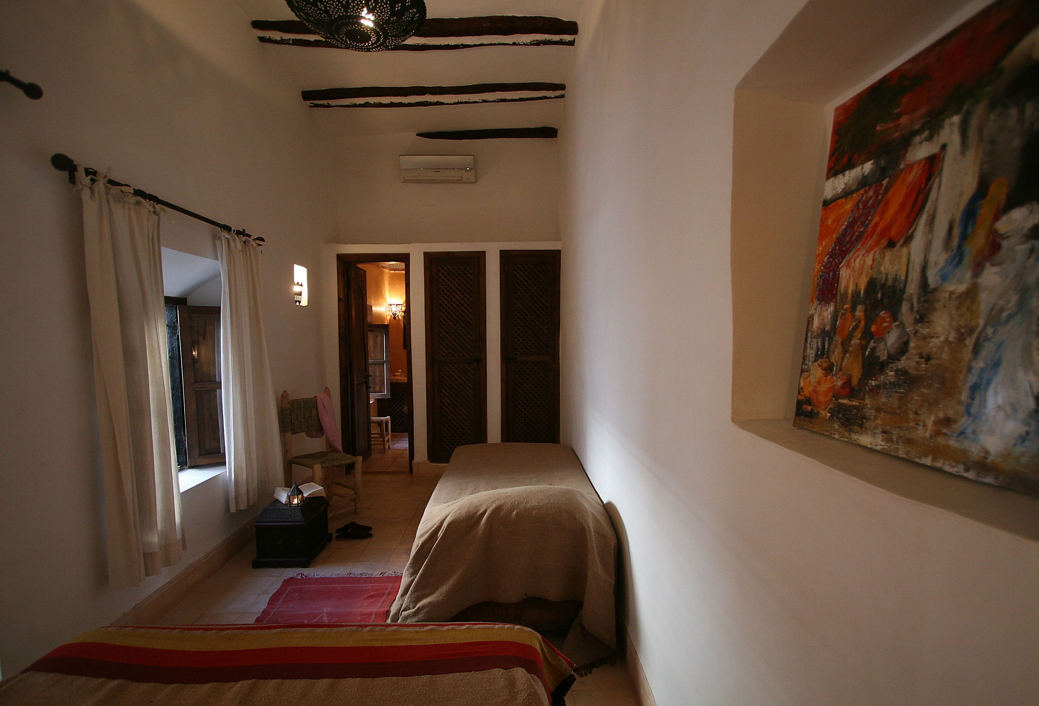 Um quarto pequeno com duas camas, um quadro na parede e uma janela com cortinas.