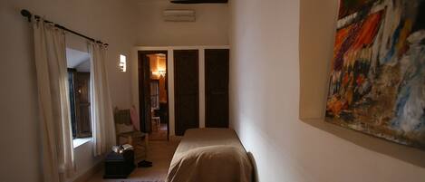 Una habitación estrecha con dos camas, un cuadro en la pared y una ventana con cortinas.