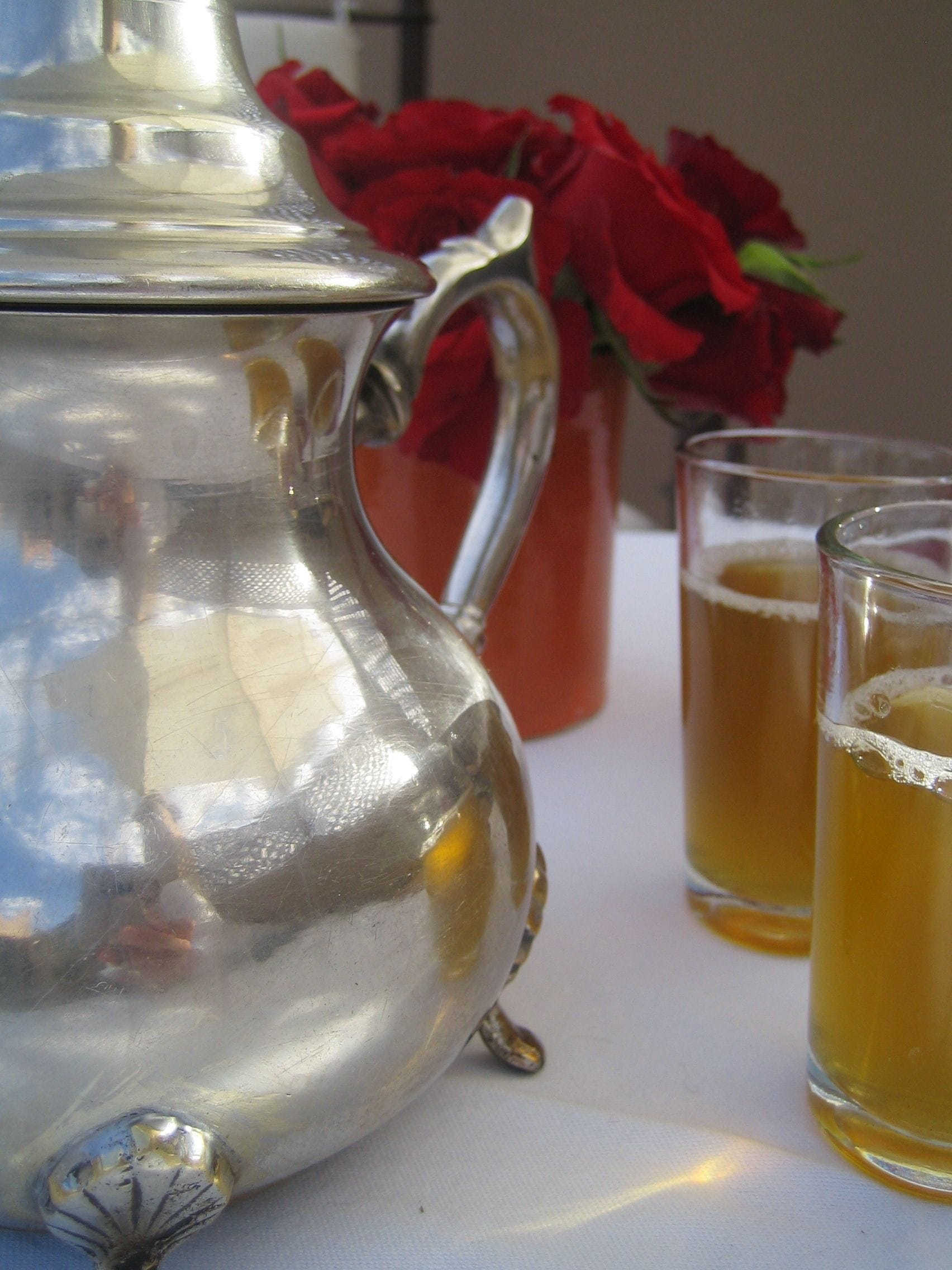 A silver teapot, two glasses of tea, and a red rose in the background.