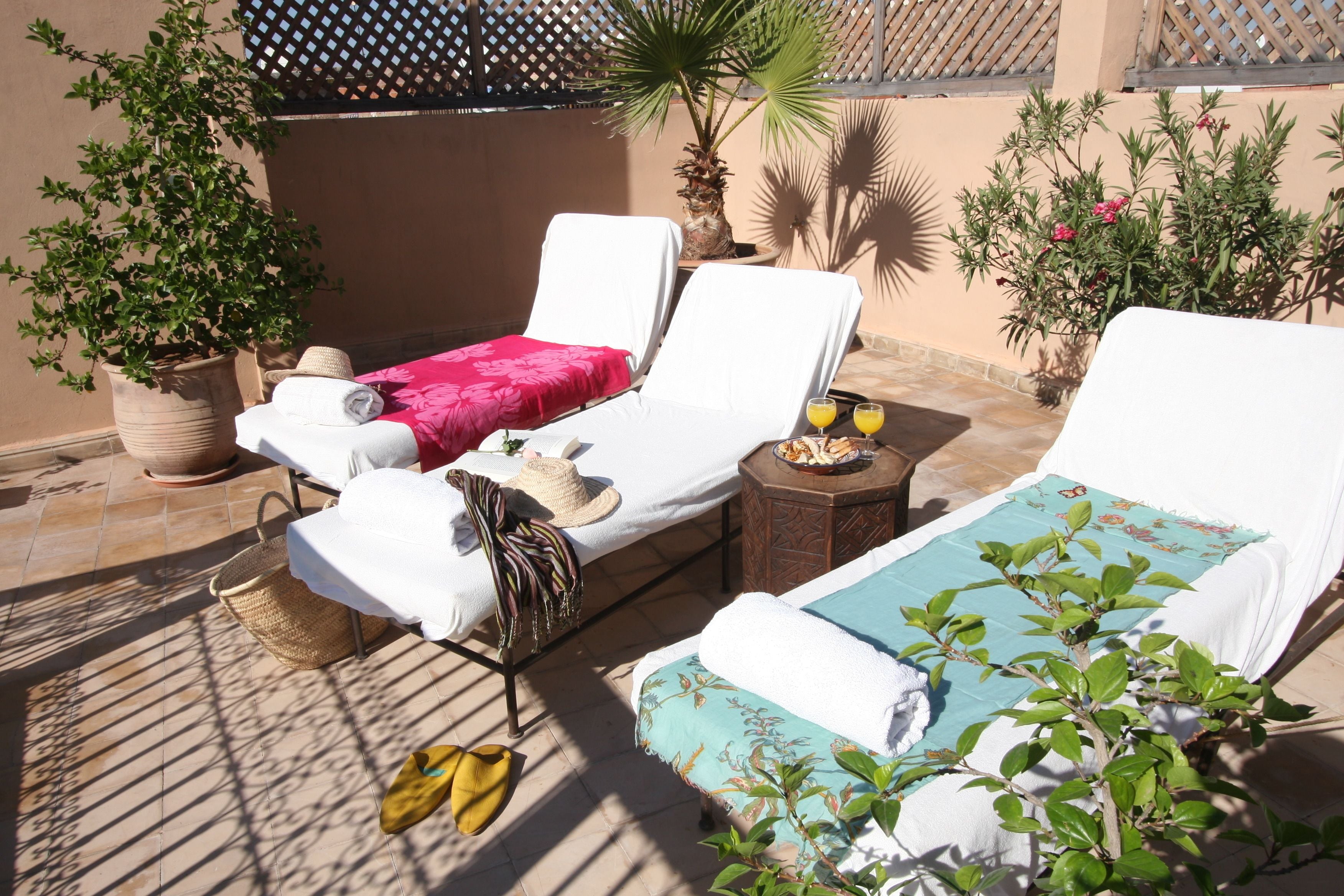 A sunlit outdoor seating area with two lounge chairs, a table with a drink, and potted plants.