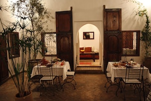 Un comedor con una mesa dispuesta para dos personas, rodeada de sillas y una planta en maceta al frente.