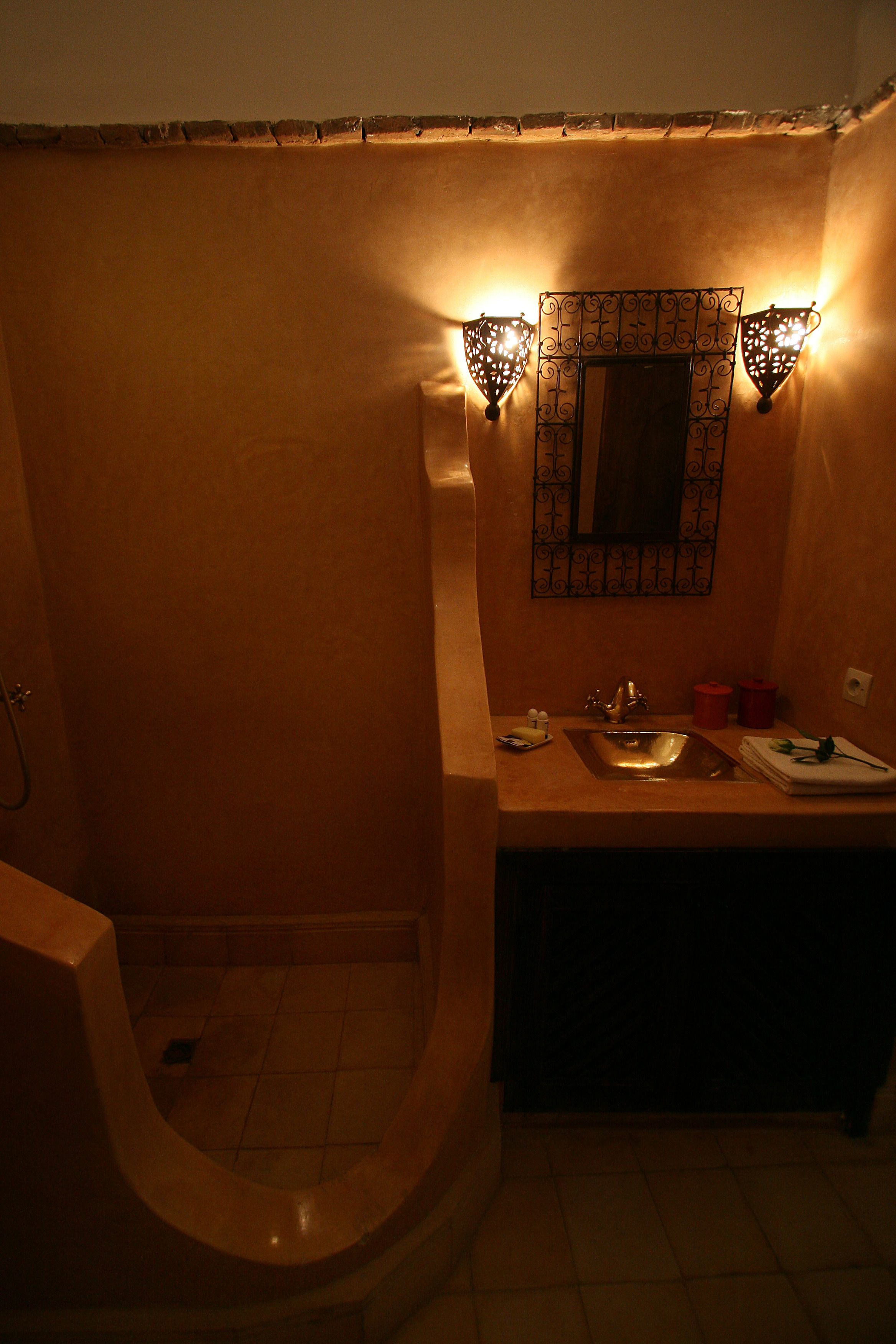 A bathroom with a curved shower, a sink with a mirror, and two wall-mounted lights.