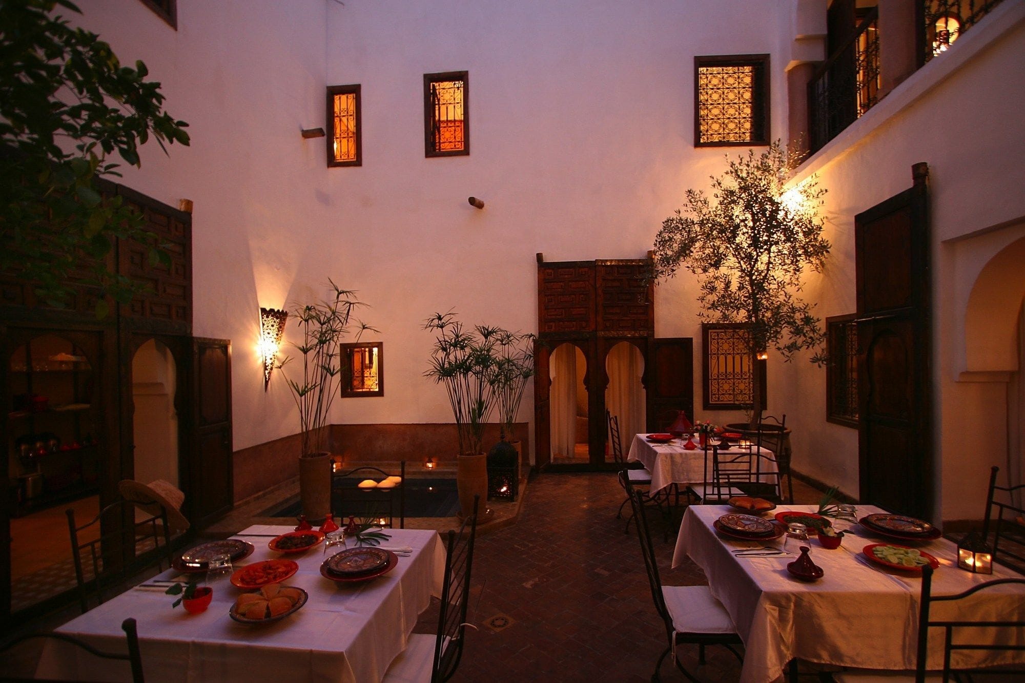 A dining area with tables set for meals, surrounded by walls with decorative windows and wall-mounted lights.