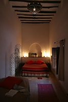 Un dormitorio con poca luz, una cama, un arco decorativo en la pared y una lámpara colgante.