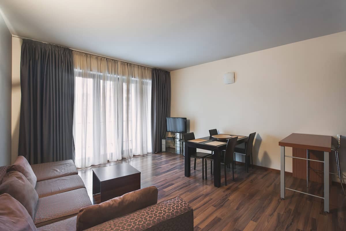 Ein modernes Wohnzimmer mit einer Sofagarnitur, einem Esstisch mit Stühlen, einem Fernseher und einem Flachbildfernseher auf einem Standfuß.