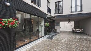 A courtyard with a car parked in a covered area, a building with a glass facade, and a hanging flower arrangement.