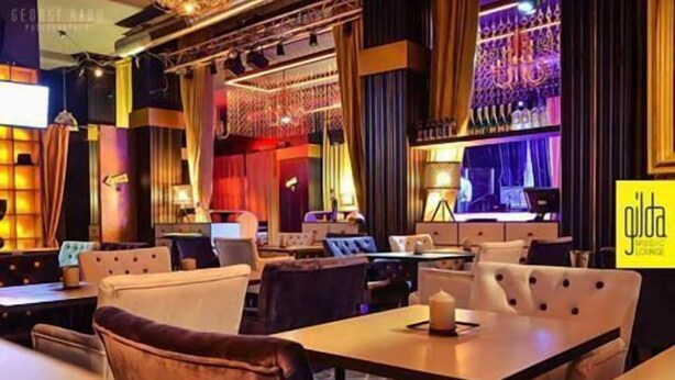 A modern lounge area with multiple seating options including sofas and tables, ambient lighting, and a decorative wall with patterns.