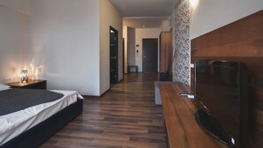 A modern hotel room with a bed, wooden flooring, a TV, and a wooden bench.