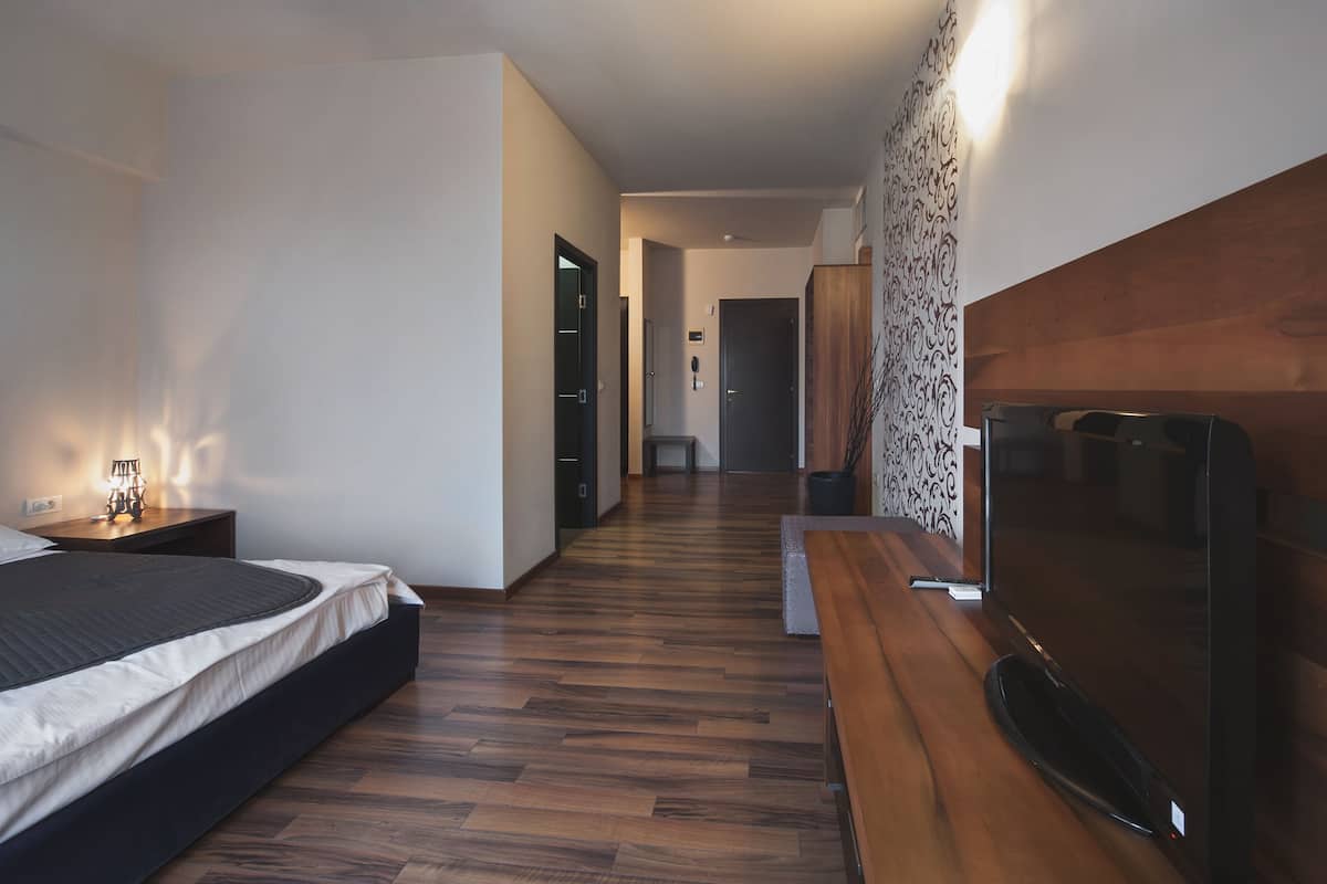 Ein modernes Hotelzimmer mit einem Bett, einem Fernseher, einer Holzbank, einem Schreibtisch und einer Wand mit Musterung.