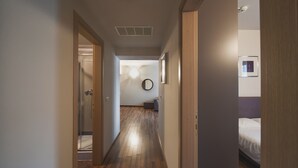 A hallway with wooden flooring, a round mirror on the wall, and a bed with white bedding in the room.