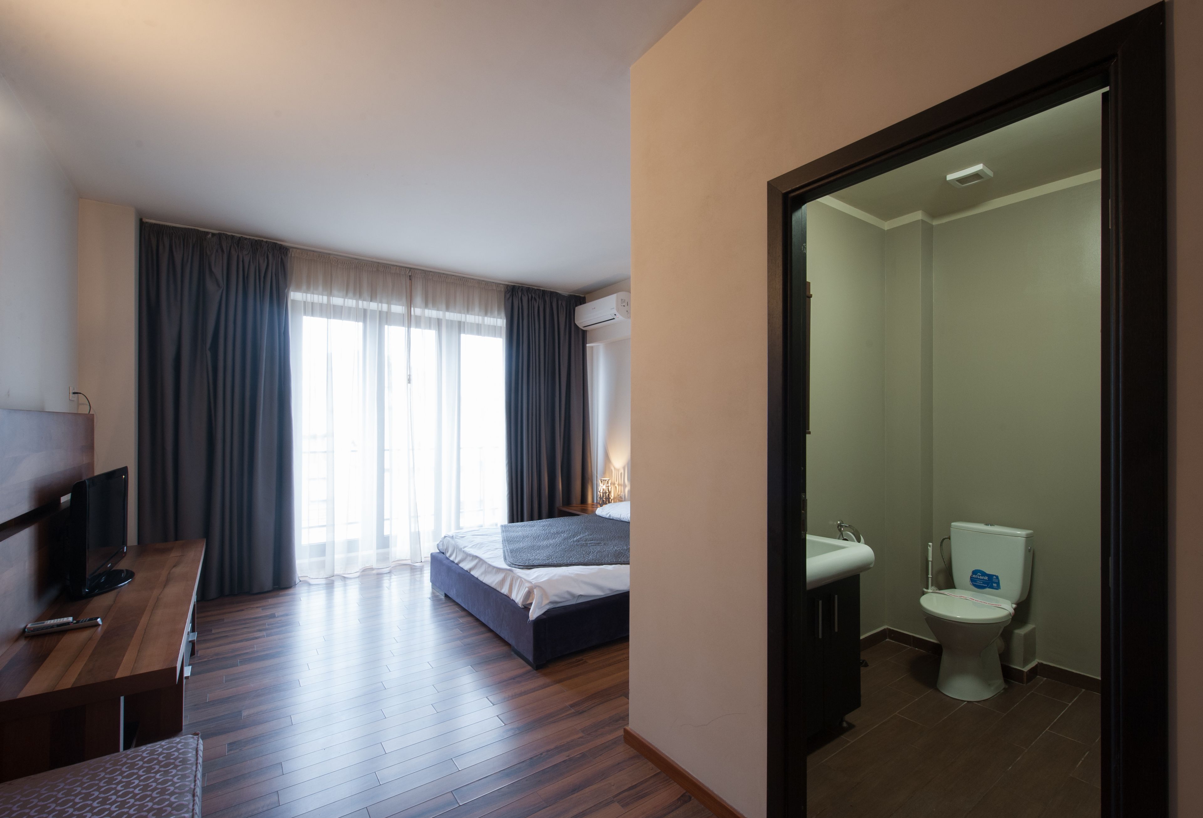 A hotel room with a bed, a desk with a TV, a bathroom with a toilet and sink.