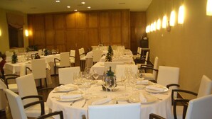 Un salón de banquetes con mesas redondas dispuestas para cenar, sillas blancas y un centro de mesa con un árbol de Navidad.