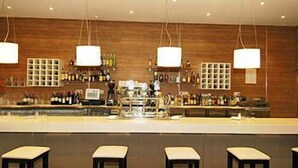Una zona de bar con una barra larga, varios taburetes, lámparas colgantes y estantes con botellas.
