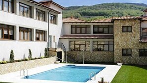 Un edificio de dos pisos con piscina, muros de piedra y un césped cuidado.