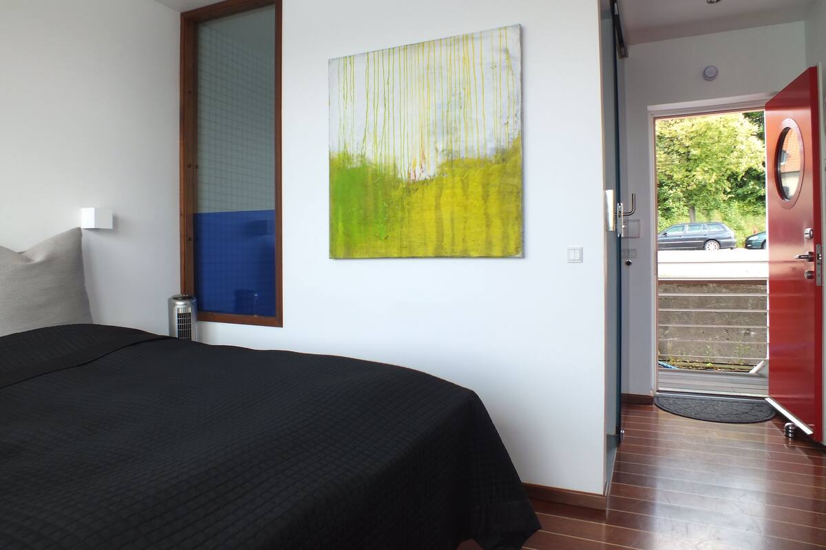 A bedroom with a bed, a painting, and a door leading to an outdoor area.