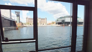 A room with a large window overlooking a river, featuring a table with a plate and a cup, and a chair. - CPH Living (Copenhagen)