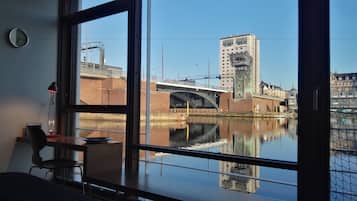 A room with a large window overlooking a canal, a bridge, and a building labeled "DANHOSTEL".