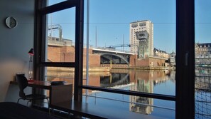 Une chambre dotée d’une grande fenêtre donnant sur un canal, un pont et un bâtiment portant l’inscription « DANHOSTEL ».