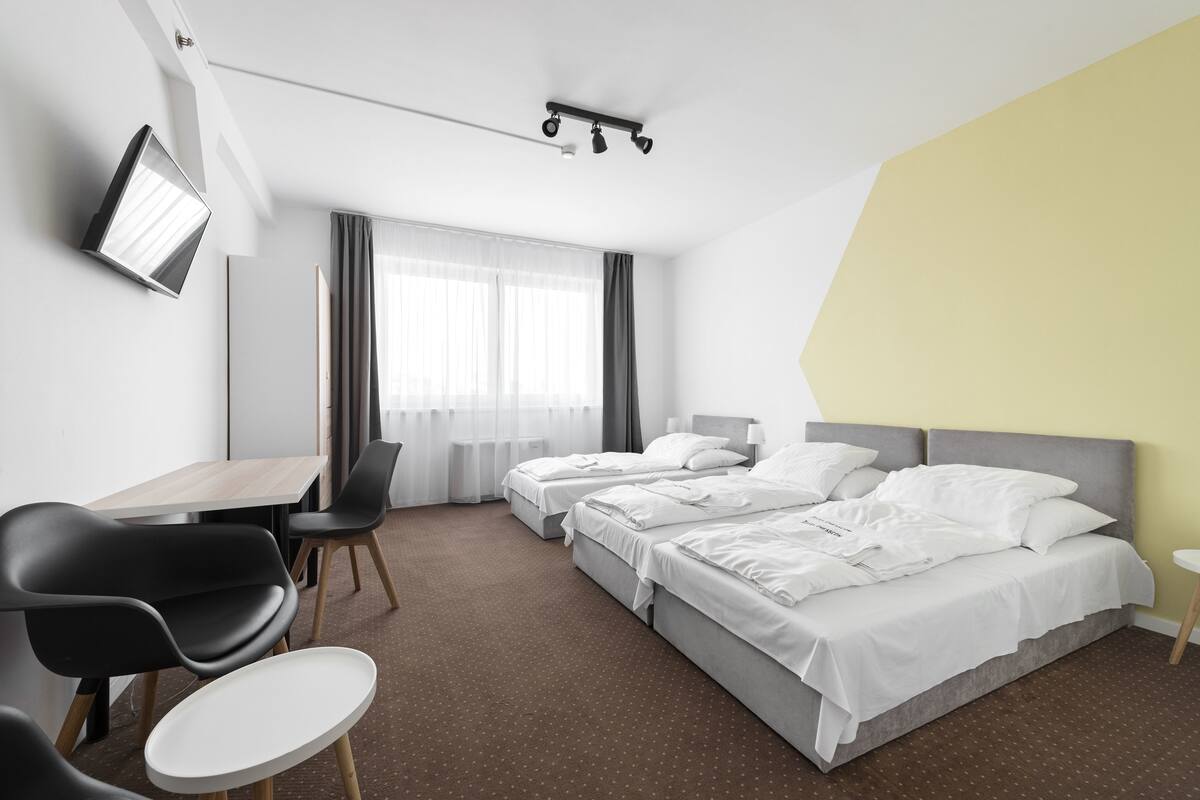 A hotel room with two beds, a desk, a chair, and a TV mounted on the wall.