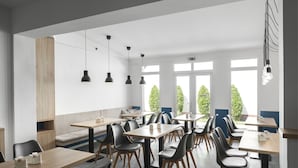 Un comedor moderno con varias mesas y sillas, ventanas amplias con vistas a zonas verdes e iluminación colgante.