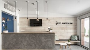 Una moderna zona de recepción de hotel, con un mostrador gris, paneles de madera, un televisor montado y luminarias colgantes.