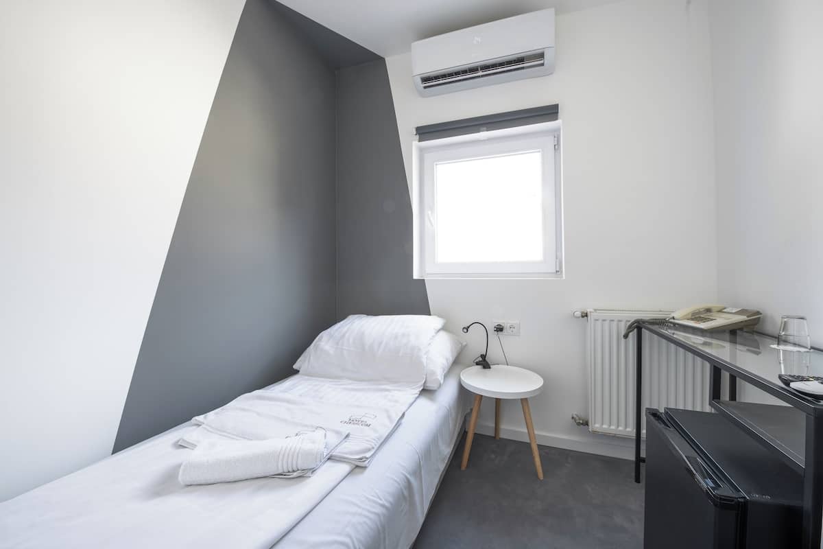 A small, modern bedroom with a bed, a bedside table, a radiator, and a window.