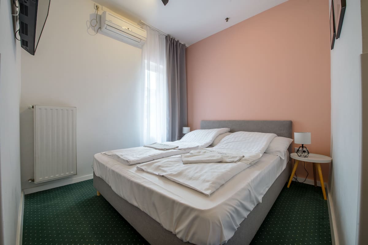 A neatly made bed with white linens, a bedside table with a lamp, and a radiator on the wall.