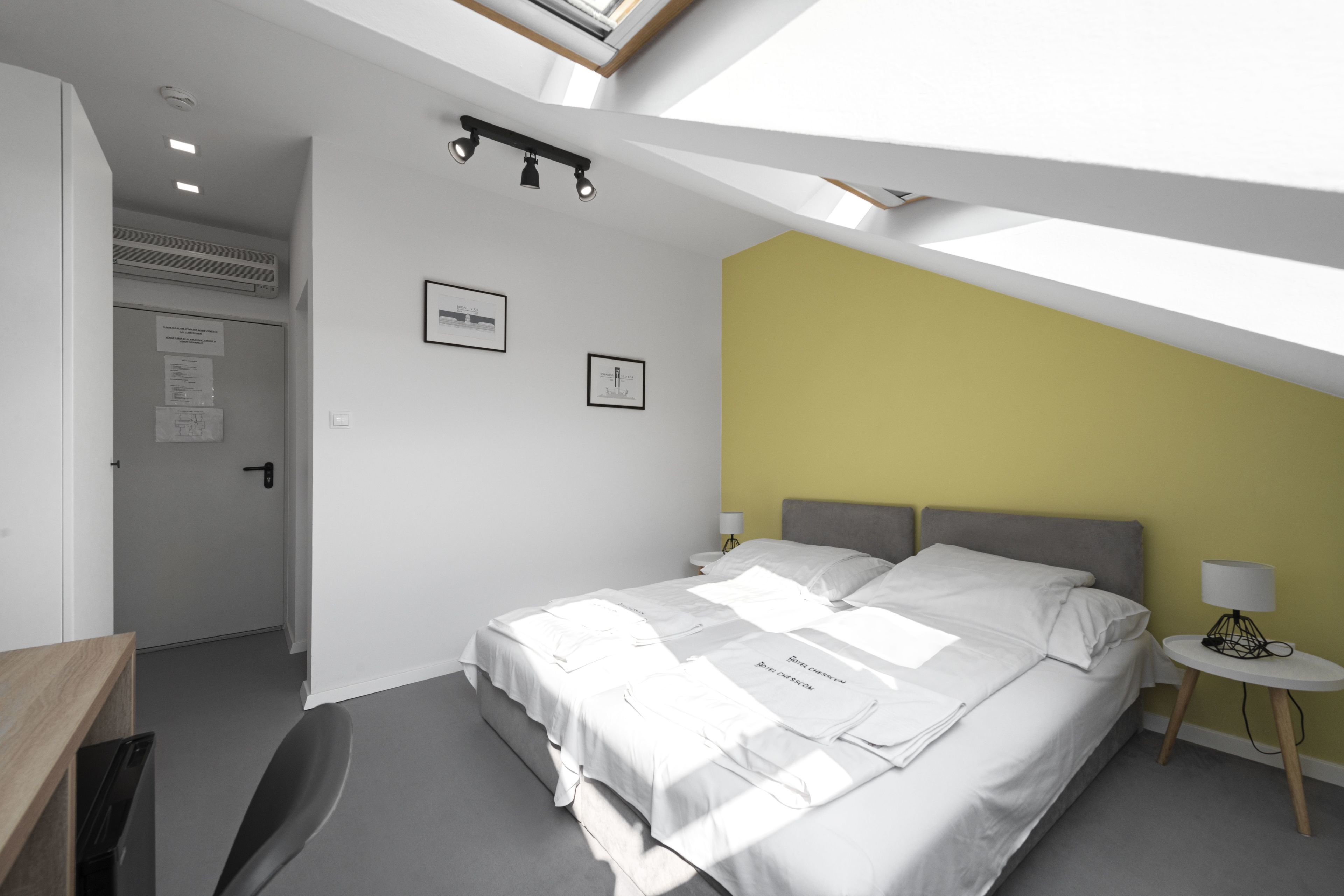 Ein modernes Schlafzimmer mit Oberlicht, einem Bett mit weißen Bettwäsche, einem Nachttisch mit Lampe und einem Schreibtisch mit Stuhl.