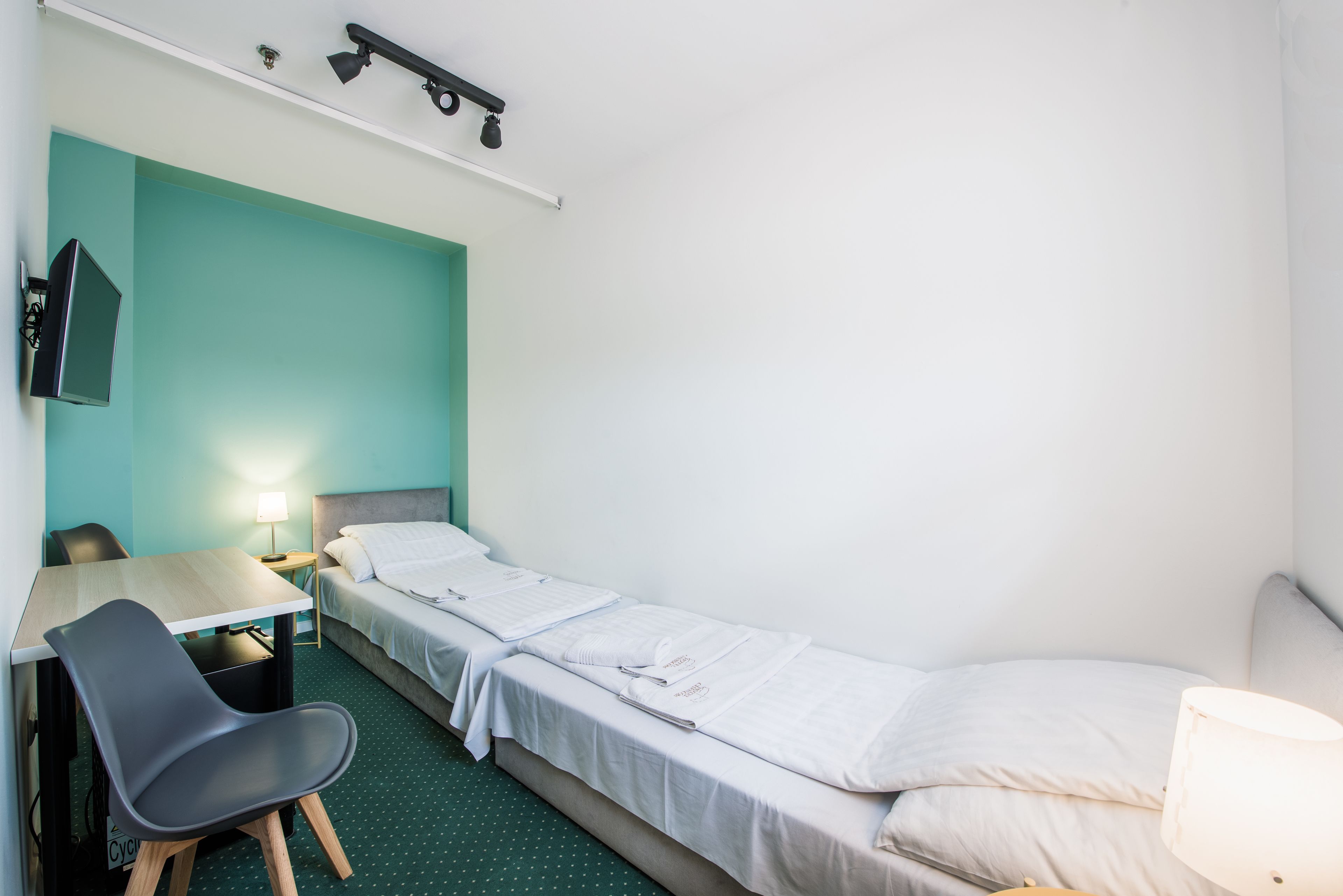 A single-bed room with a desk, chair, and a TV mounted on the wall.