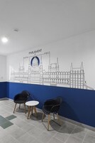 Un vestíbulo con un mural de un edificio, dos sillas negras, una mesa redonda pequeña y una pared azul decorativa.