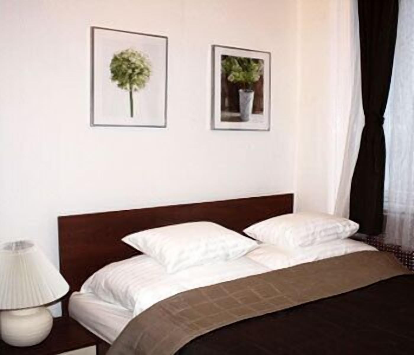 A hotel room with a bed, white bedding, a nightstand with a lamp, and two framed pictures on the wall.