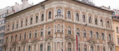 Un edificio histórico con fachada en esquina, con múltiples ventanas y detalles arquitectónicos ornamentales.