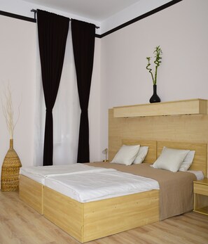 A modern bedroom with a wooden bed, black curtains, a bedside lamp, and a vase with a plant. - Centrooms House (Budapest)