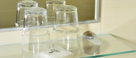 Une salle de bain avec une étagère en verre sur laquelle sont posés plusieurs verres transparents, un lavabo blanc et un miroir.