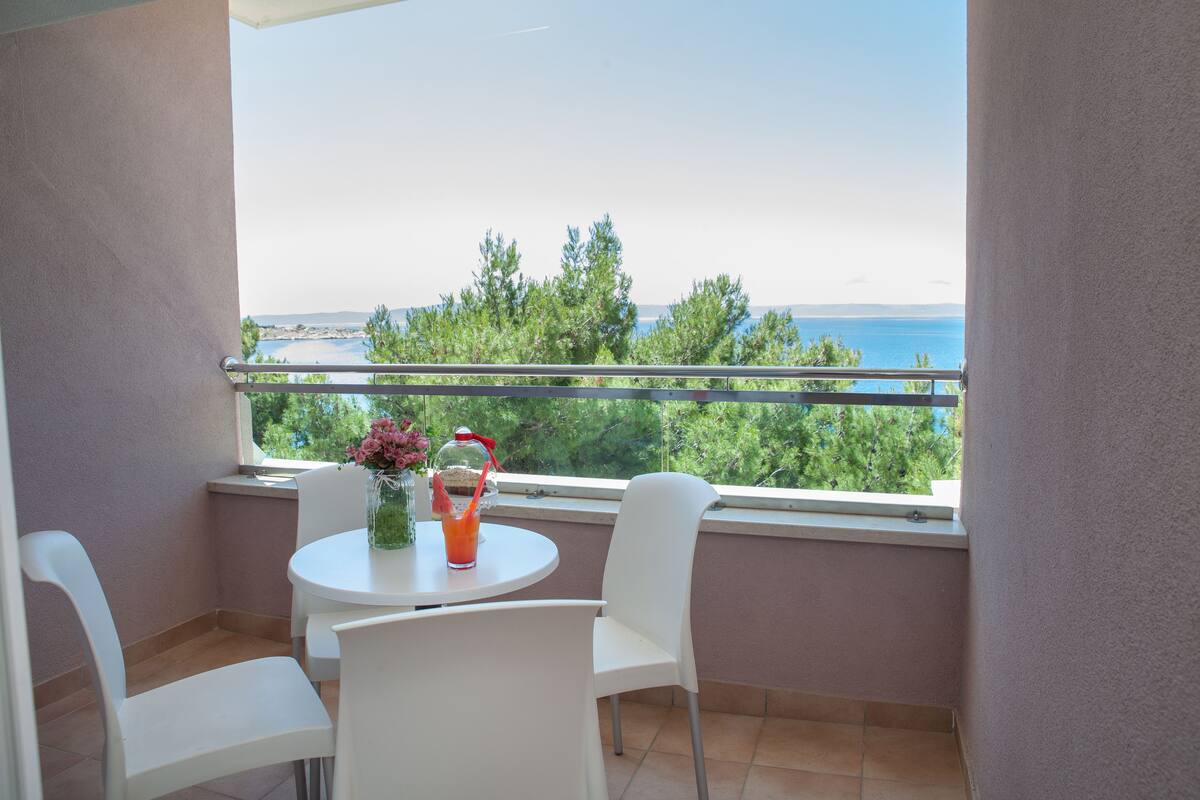 A balcony with a table and chairs, overlooking a scenic view of the sea and greenery.