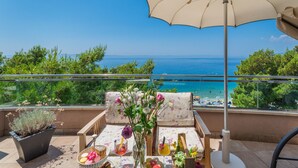 A balcony with a view of the sea, a table with drinks and snacks, and a large umbrella. - Hotel Maritimo (Makarska)