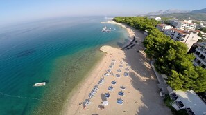 Vista aérea de una playa con filas de tumbonas y un barco anclado cerca de la orilla.