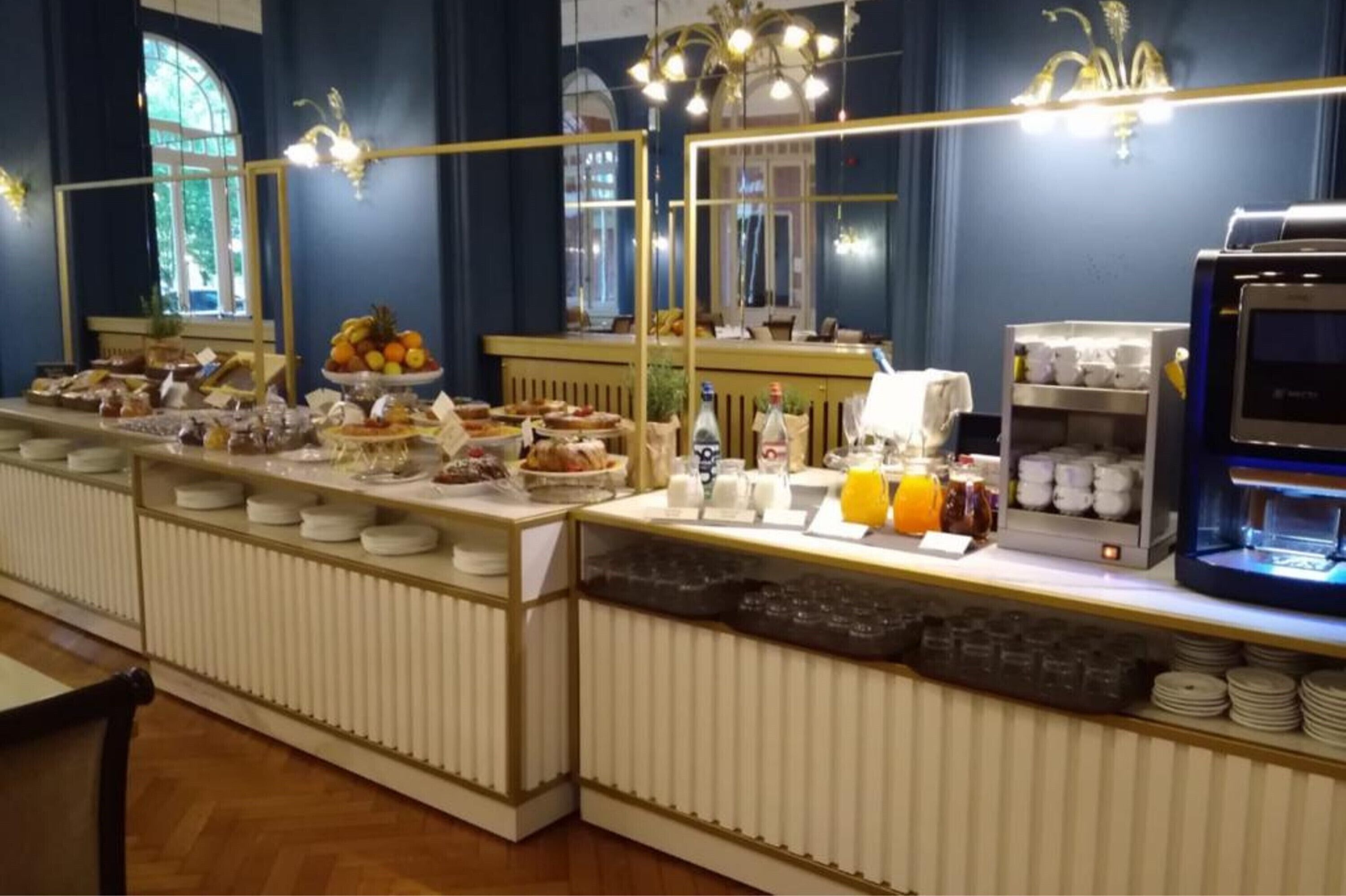 A buffet setup with various food items, a coffee machine, and a refrigerator.