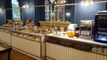 A buffet setup with various food items, a coffee machine, and a refrigerator.