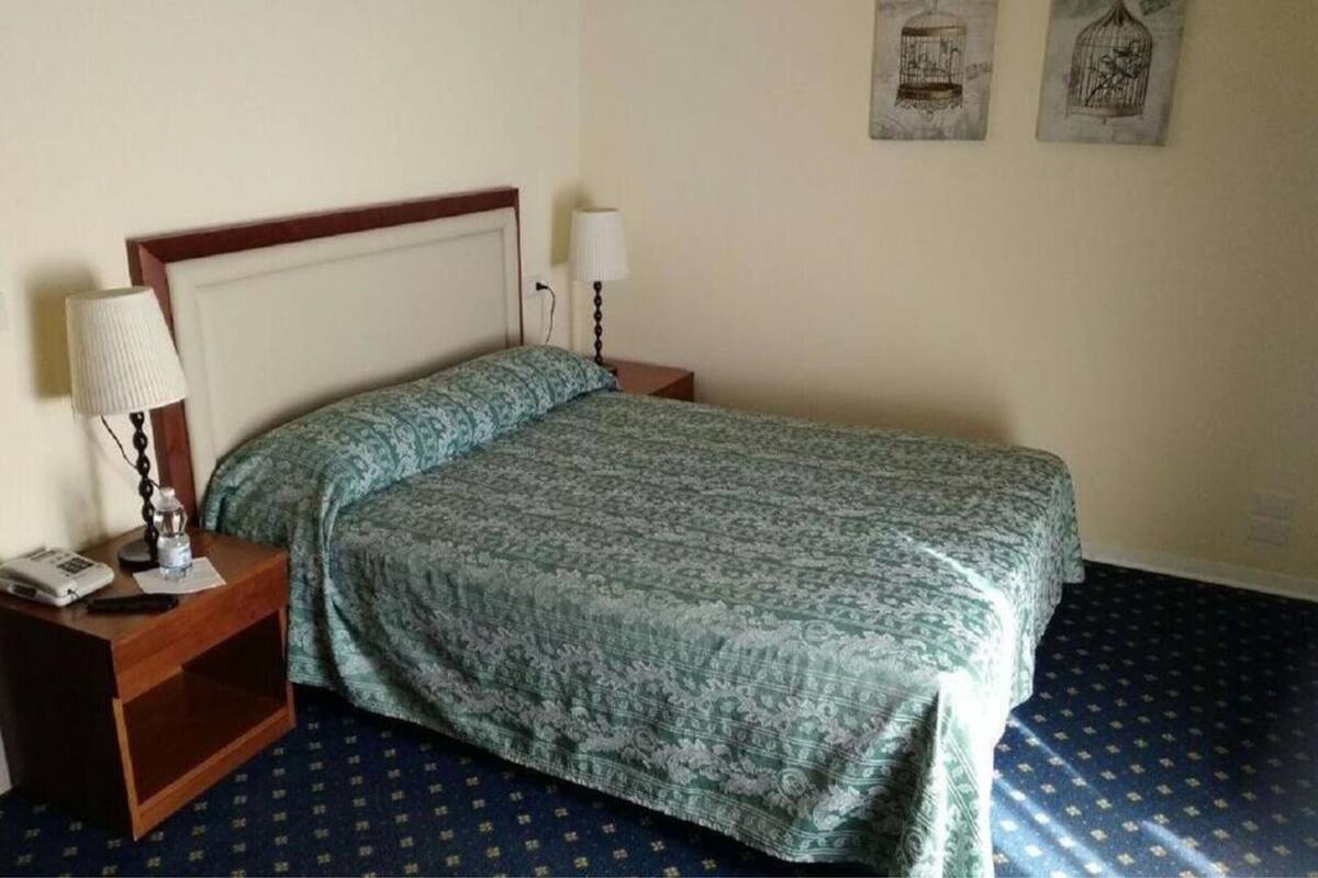 A single bed with a patterned bedspread, a bedside lamp, and a nightstand with a phone and a lamp.