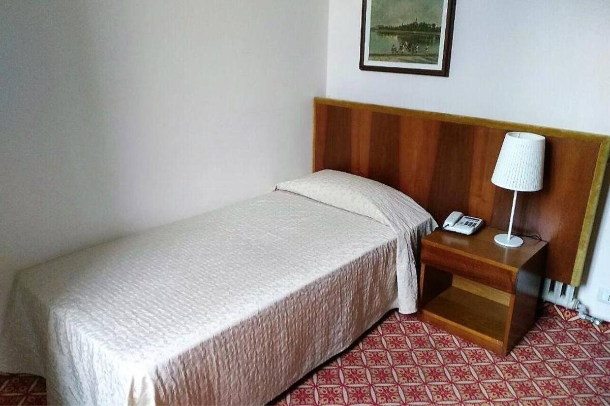 A single bed with a wooden headboard, a bedside table with a lamp, and a telephone.