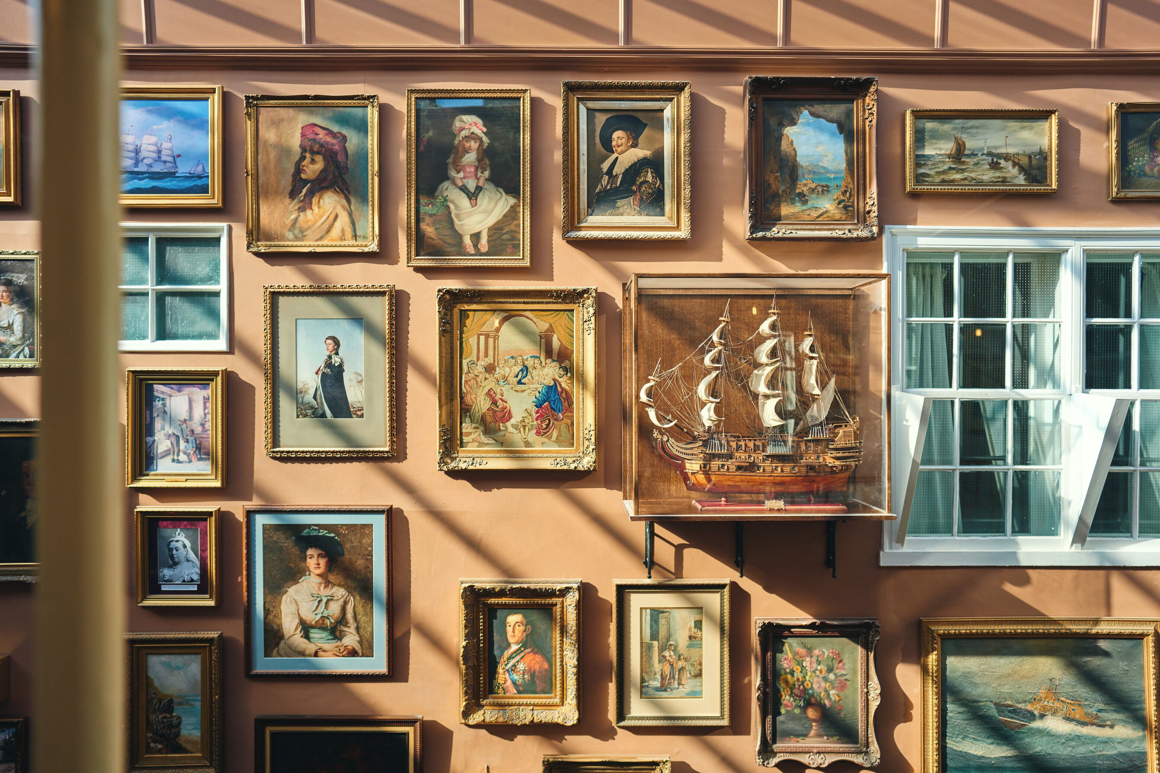 Un mur orné de divers tableaux encadrés, notamment des portraits et des scènes maritimes.