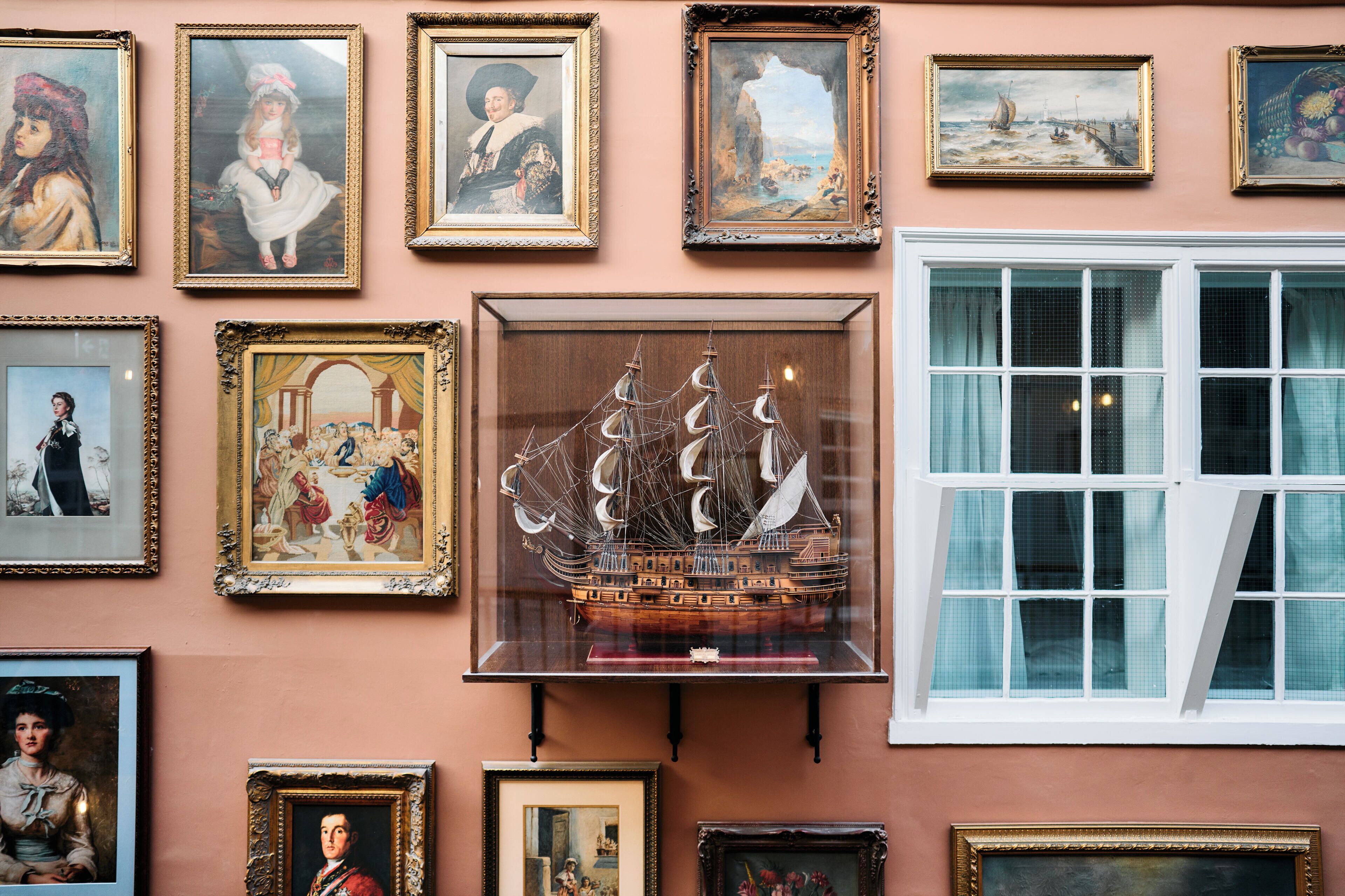 A wall with various framed artworks and a model ship.