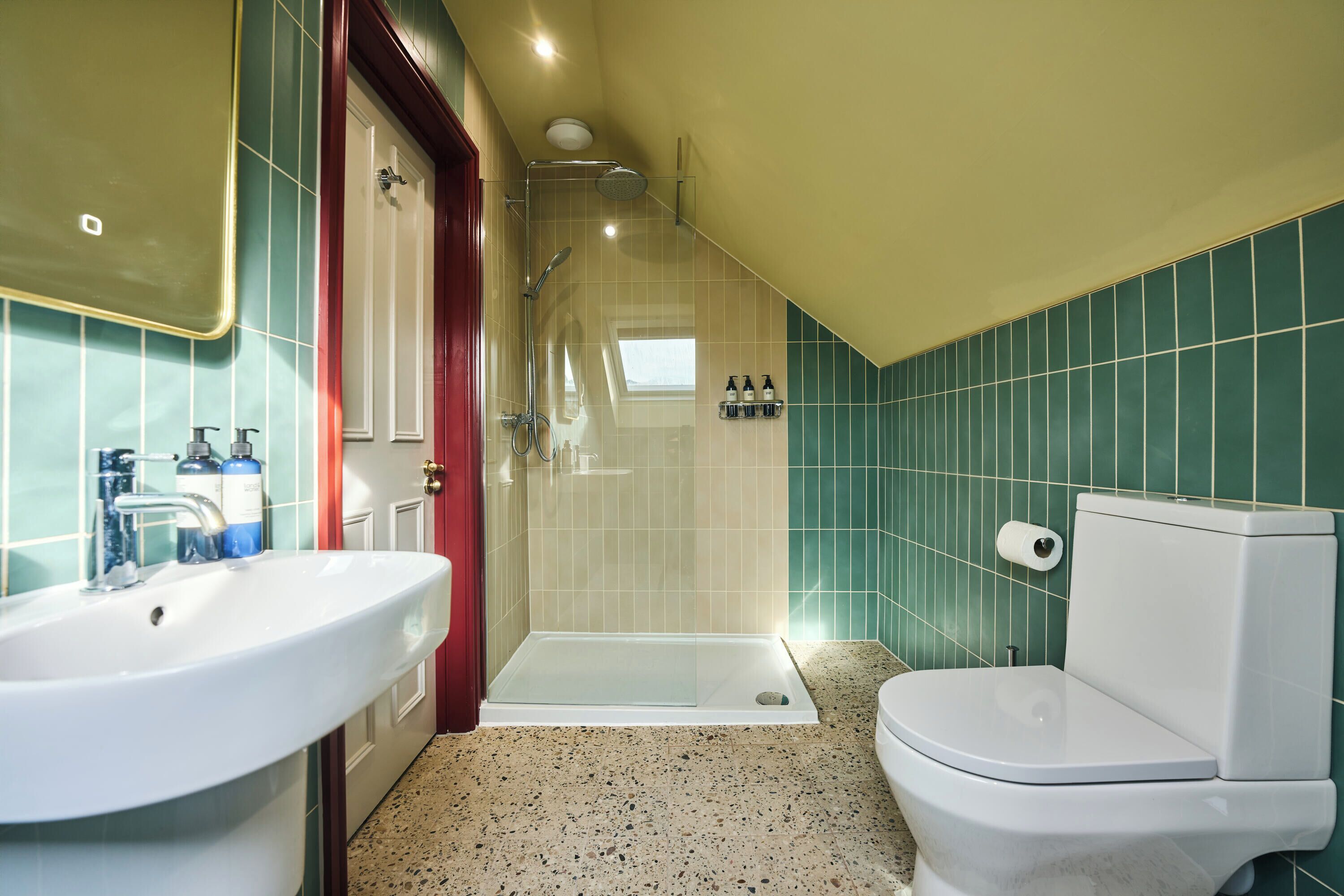 A bathroom with a sink, toilet, shower, and a tiled wall.