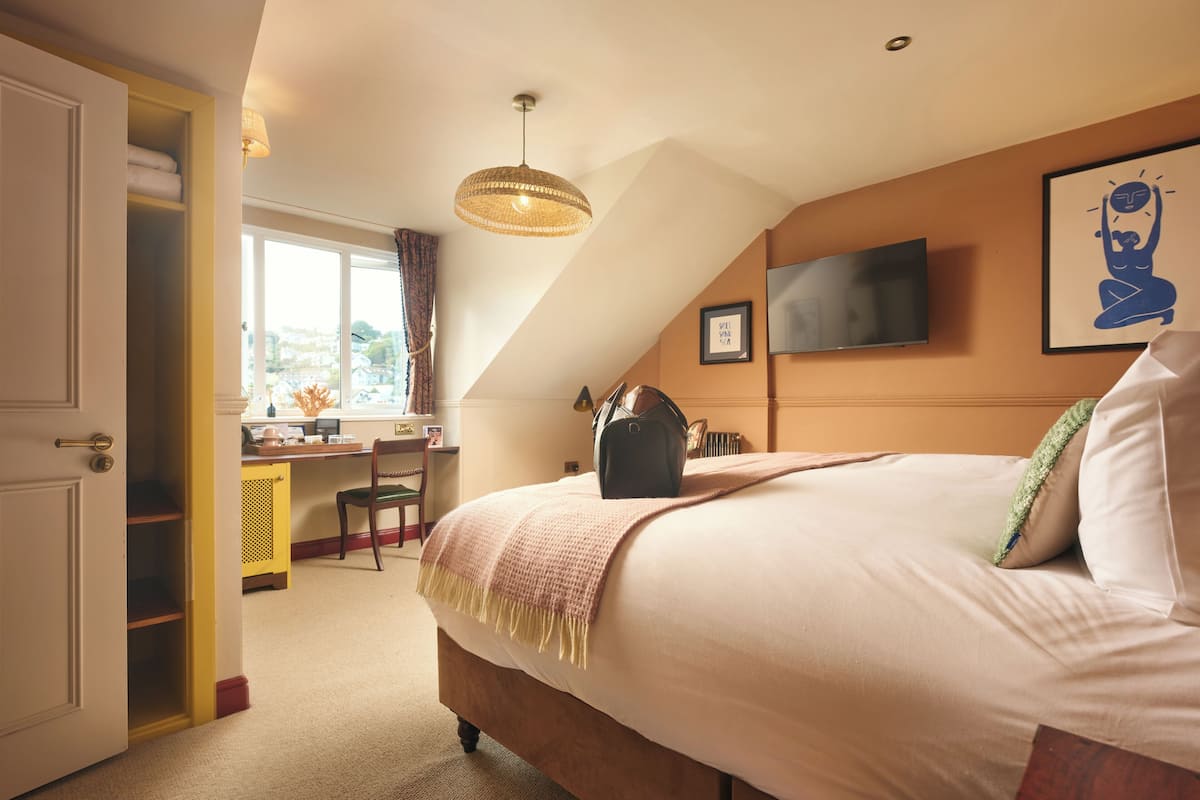 A bedroom with a bed, a desk, a chair, a television, and a window.