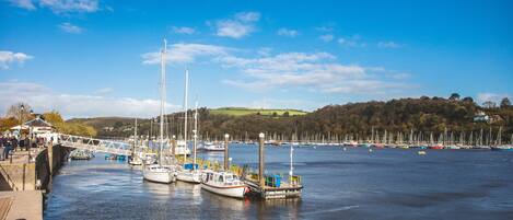 A harbor with boats docked along the pier, a bridge, and a backdrop of hills and trees.